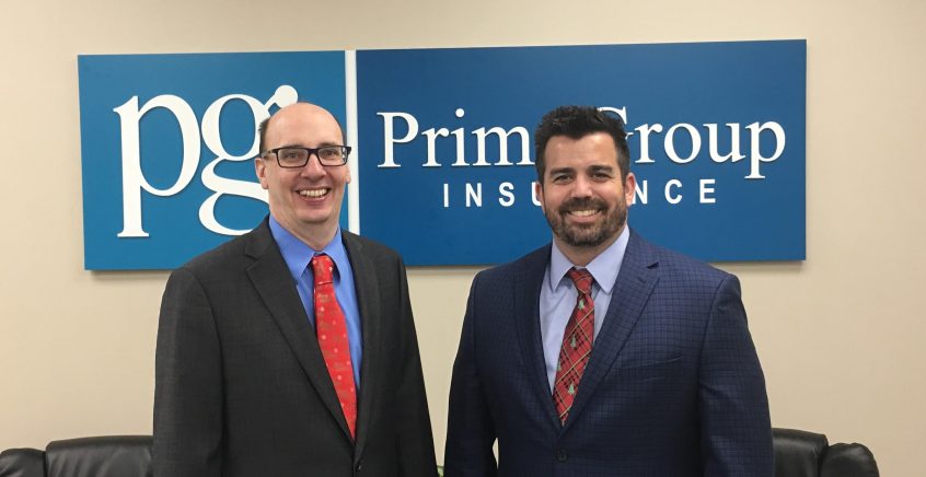 2 people posing in front of a prime group insurance sign