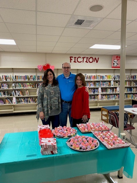 3 people behind a table full of cupcakes